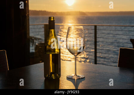 Seul verre de vin blanc coulé sur une plage accueil table avec coucher de soleil en arrière-plan. Banque D'Images