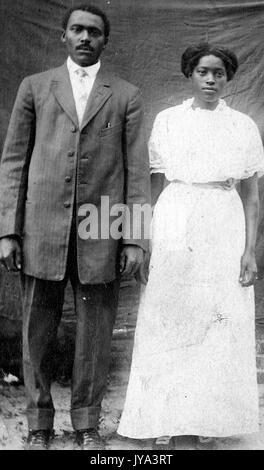 African American couple posant pour des photographies en face d'une feuille, la femme vêtue d'une robe blanche, un homme portant un costume et une cravate, 1915. Banque D'Images