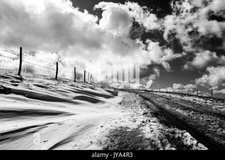 Une route de montagne avec de la neige sur le côté, sous un ciel profond avec des nuages blancs Banque D'Images