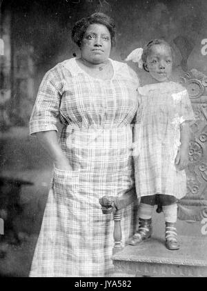 Mère afro-américaine et de la jeune fille qui pose pour un portrait, la femme porte une robe, la jeune fille portant une robe de contrepartie et debout sur une chaise, faisant d'elle la même hauteur que sa mère, 1912. Banque D'Images