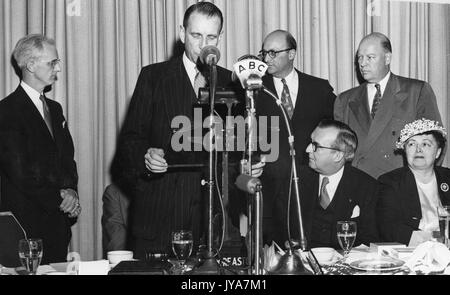 Animateur de télévision américain Lynn Poole stands et observe tandis que Edward semaines, éditeur de magazine, lit une citation pour l'émission de télévision The Johns Hopkins science review, d'autres invités assis et à la recherche sur, 1953. Banque D'Images