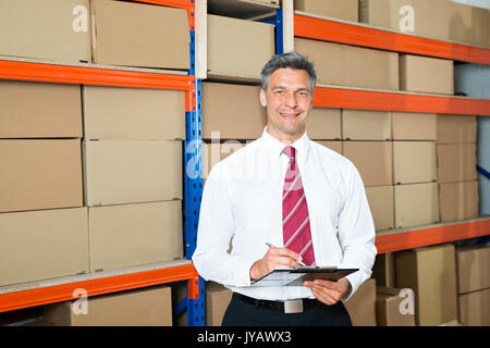 Happy Manager Writing On Clipboard In Distribution Warehouse Banque D'Images