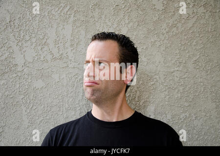 L'homme en face d'un fond beige faisant un visage mécontent à la vers la gauche. Banque D'Images