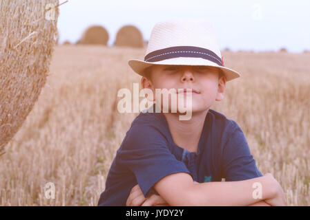 Jeune garçon de pays dans la région de hat près de meules au coucher du soleil en été. Concept d'été, des vacances actives à l'extérieur.Les loisirs avec les enfants lors des chaudes journées d'été. Banque D'Images