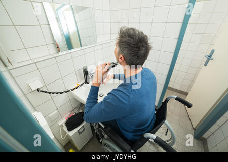 Homme handicapé en fauteuil roulant sur la barbe de fraisage dans la salle de bains Banque D'Images