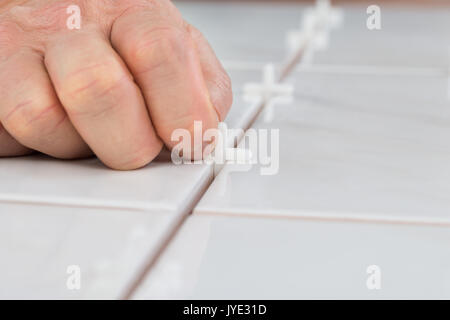 Close-up of a person's Hand de placer les entretoises entre les carreaux de sol en céramique Banque D'Images