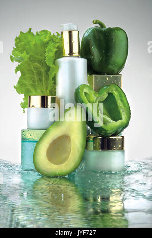 Photo créative de différents pots cosmétiques et les légumes verts dans de l'eau splash. Banque D'Images
