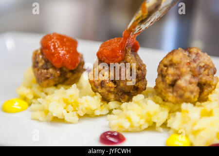 Chef de mettre la sauce tomate sur les boulettes de pommes de terre sur un tapis de Banque D'Images