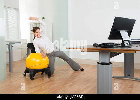 Young Businesswoman faisant Exercice Fitness Pilates ballon jaune sur In Office Banque D'Images