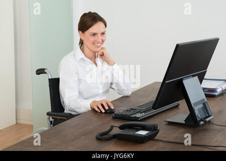 Happy Businesswoman Sitting on Fauteuil roulant tout en travaillant sur l'ordinateur au bureau Banque D'Images