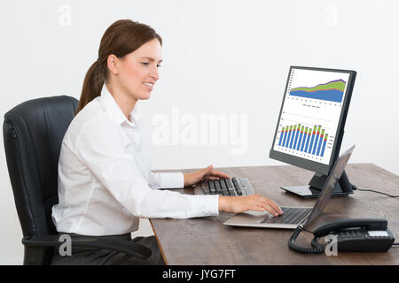 Young Businesswoman Working sur les rapports statistiques affichées sur Computer in Office Banque D'Images