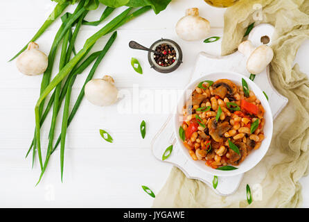 Ragoût de haricots blancs avec les champignons et les tomates avec sauce épicée dans un bol blanc. Vue d'en haut. Mise à plat Banque D'Images
