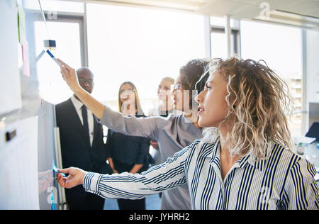 Les activités axées sur le groupe de collègues ensemble de réflexion sur un tableau blanc pendant une séance de stratégie dans un bureau moderne et lumineux Banque D'Images