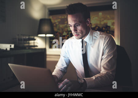 Pensive businessman typing assis à l'ordinateur portable dans le bureau le soir. Banque D'Images