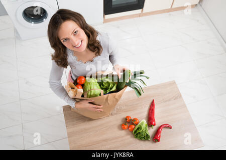 High Angle View Of Cheerful Woman with grocery Bag In Kitchen Banque D'Images