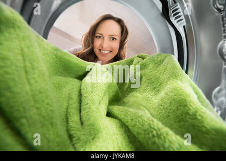 Happy Woman Putting Green Towel voir de l'intérieur du lave-linge appareil Banque D'Images