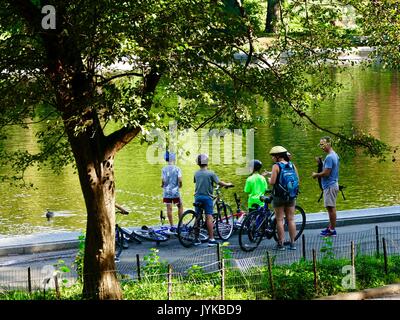 Famille avec bicyclettes - mère, père, fils, s'arrête pour prendre une pause à côté d'un étang dans Central Park, New York, NY, USA. Banque D'Images