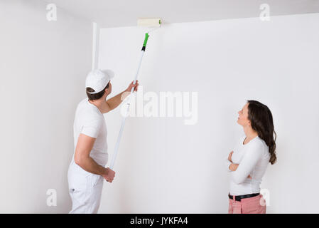 Jeune femme à la peinture peintre à blanc sur mur de chambre Banque D'Images