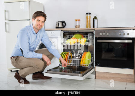 Jeune homme heureux la mise en tablette du savon lave-vaisselle lave-vaisselle détergent fort dans la chambre Cuisine Banque D'Images