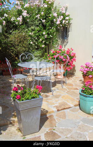 Terrasse fleurie avec mobilier de jardin gris et quelques pots de géraniums au printemps Banque D'Images