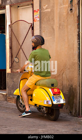 Man getting sur scooter jaune jaune portant des shorts et tee-shirt vert à Tolède, Espagne Banque D'Images