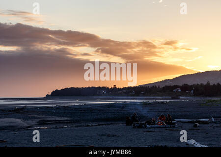 Campeurs se relaxant et profiter du feu de camp de plage au coucher du soleil sur une plage déserte avec du bois flotté Banque D'Images