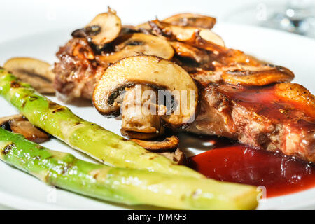 Ribeye Steak grillé juteux délicieux avec les champignons et les asperges vertes, sauce rouge, sur une assiette, portrait, gros plan Banque D'Images