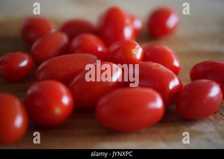 Une douzaine de fraîchement lavés, prêts à être haché, tomates raisins rouges sur une planche à découper en bois. Banque D'Images