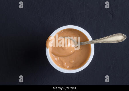 Vue de dessus d'arrière-plan de Yogourt aromatisé au caramel de yogourt en synthétique avec petite cuillère en argent isolé sur fond noir - close up image avec Banque D'Images