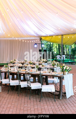 Célébration, restauration, propreté concept. brun riche tables en bois avec tidy et bouquets de fleurs debout sous une grande tente et attendre les invités Banque D'Images