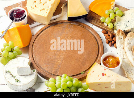 Différents types de fromage avec du raisin, de la confiture, du pain et des noix sur table en bois. Banque D'Images