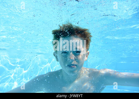 Adolescent aux cheveux auburn, sous l'eau dans une piscine, à la caméra en Banque D'Images
