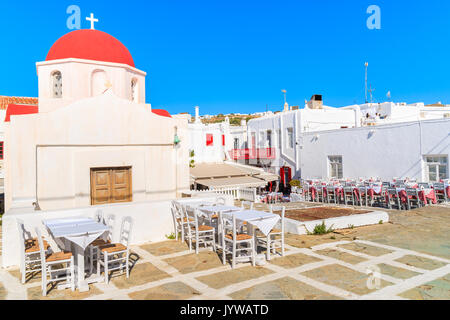 Grec typique église blanche et de la taverne des tables dans la ville de Mykonos, Grèce Banque D'Images