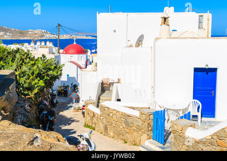Blanc typique maison grecque avec porte bleue et l'église dans la distance dans la belle ville de Mykonos, Cyclades, Grèce Banque D'Images