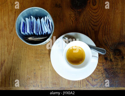 Un espresso à côté d'un récipient contenant des paquets d'égales, un substitut du sucre, sucre brun et deux paquets sur le comptoir de bois Banque D'Images