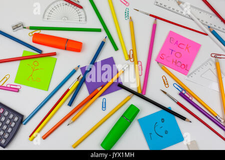 Retour à l'école note sur un coussin rose parmi des crayons et du papier des clips sur un bureau blanc Banque D'Images