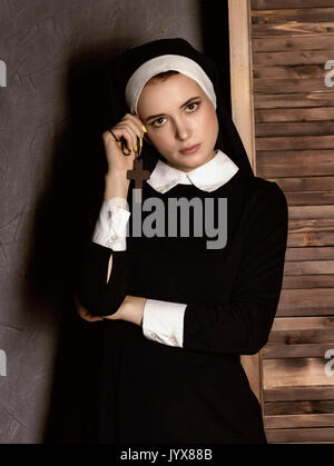 Humble jeune belle nun in robes tenant une croix sur fond gris Banque D'Images