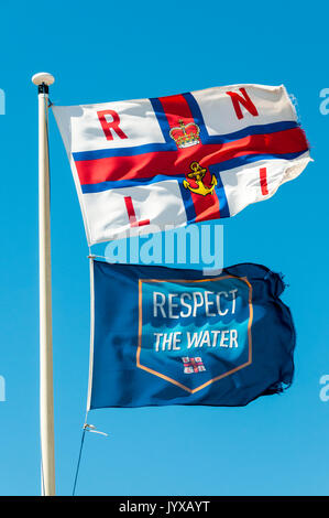 L'eau et le respect de la RNLI drapeaux au vent à l'extérieur de la station de sauvetage de dormeur. Banque D'Images