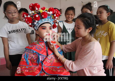 Shijiazhuang, Province de Hebei en Chine. Août 21, 2017. Un enseignant ne maquillage facial pour un peu d'opera performer dans une école primaire du canton, district de Feixiang Tiantaishan de Handan City, province de Hebei en Chine du nord, le 21 août, 2017. Le ministère de l'éducation du district de Feixiang a organisé diverses activités d'enrichissement de la vie des élèves les vacances d'été. Credit : Mu Yu/Xinhua/Alamy Live News Banque D'Images