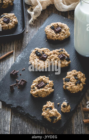 Des cookies à l'avoine et aux raisins avec du chocolat et du lait sur fond d'ardoise. Selective focus, tonique libre Banque D'Images