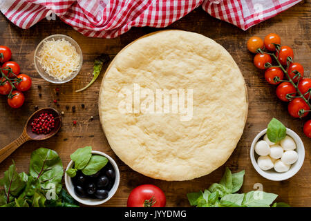 Pâte à pizza préparée, olives noires, basilic, bettes, poivre, tomates, mozzarella et parmesan sur table en bois rustique. Vue d'en haut Banque D'Images
