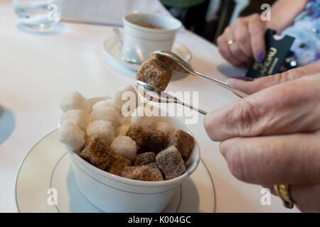 Woman taking matières brown sugar cubes avec des pinces d'argent à le roux at the landau l'hôtel Langham, 1C Portland Pl, Marylebone, London W1B 1JA, UK Banque D'Images