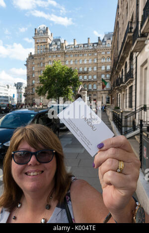 Femme tenant une carte du restaurant Le Roux at the Landau avec l'hôtel Langham dans l'arrière-plan Banque D'Images