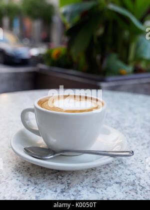 L'art en forme de cœur sur un cappuccino avec un téléphone sur une table en marbre. face à l'extérieur côté rue d'un café Banque D'Images