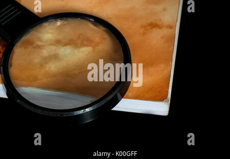 Loupe en haut d'un livre fermé, avec couvercle orange, en haut d'une surface en verre réfléchissant noir Banque D'Images