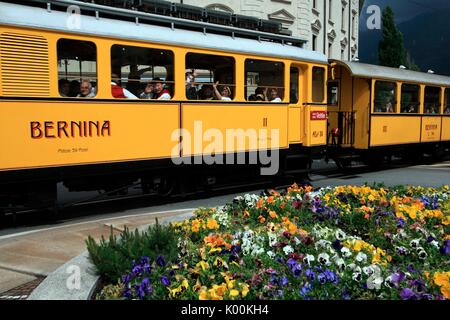 Jaune historique wagons de la Bernina Express traversant les rues à Tirano près d'un parterre de fleurs, la Valtellina, Italie Europe Banque D'Images