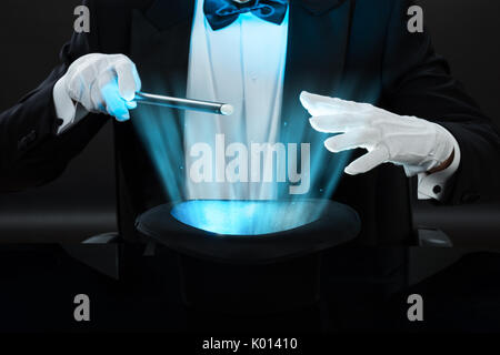 Au milieu du magicien holding baguette magique plus allumé hat sur fond noir Banque D'Images