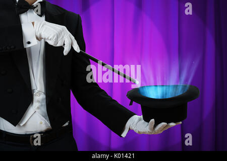 Au milieu du magicien holding baguette magique plus allumé hat contre rideau pourpre Banque D'Images