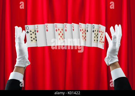 Les mains coupées de magicien de trick avec cartes contre rideau rouge Banque D'Images