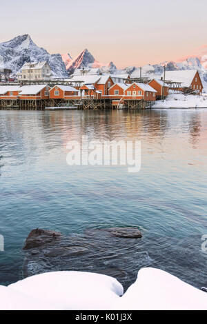 Les couleurs de l'aube les cadres de maisons de pêcheurs entouré de sommets enneigés Sakrisøy Reine Nordland îles Lofoten Norvège Europe Banque D'Images